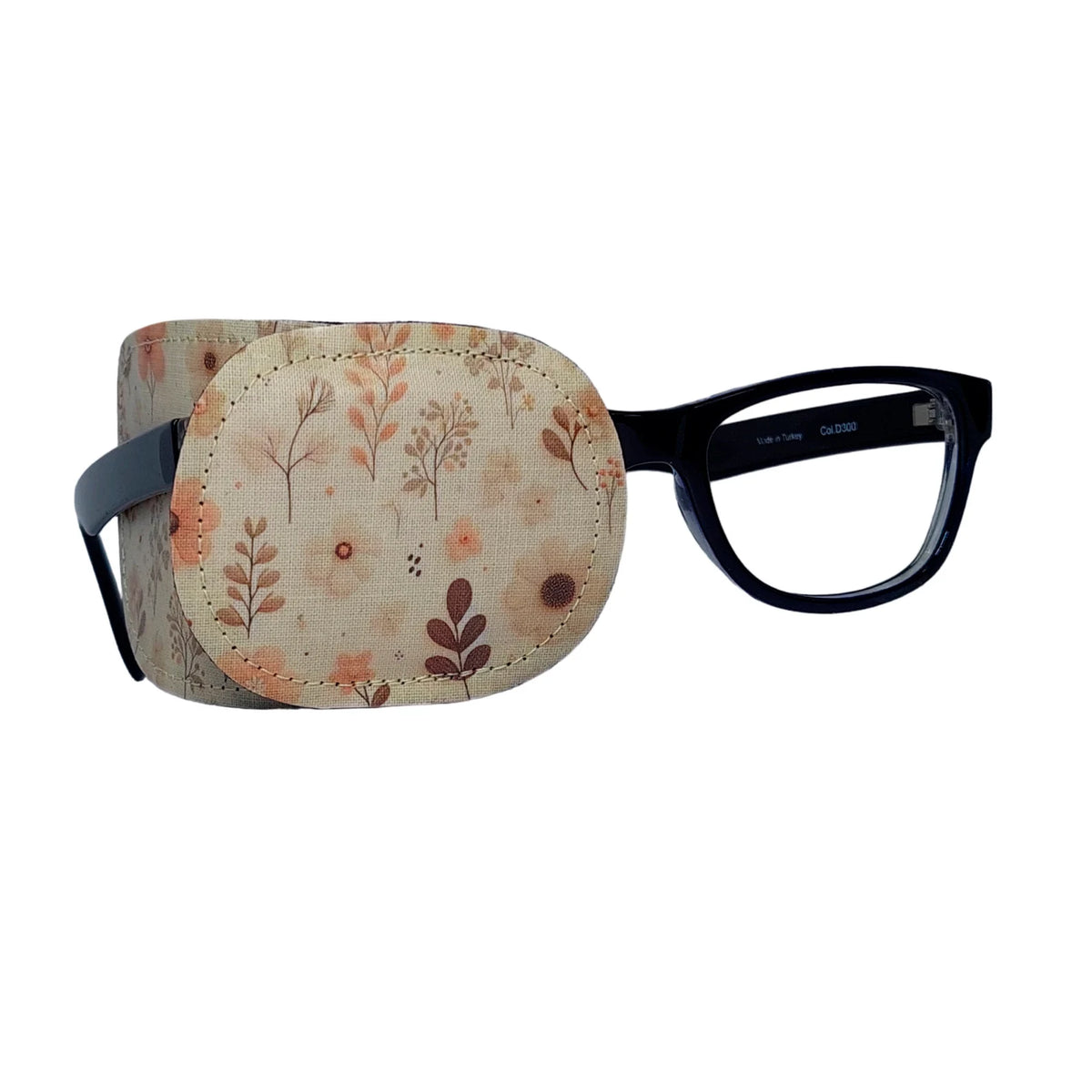 Cream fabric eye patch with wildflower and botanical design in soft corals and browns, shown on black-framed glasses